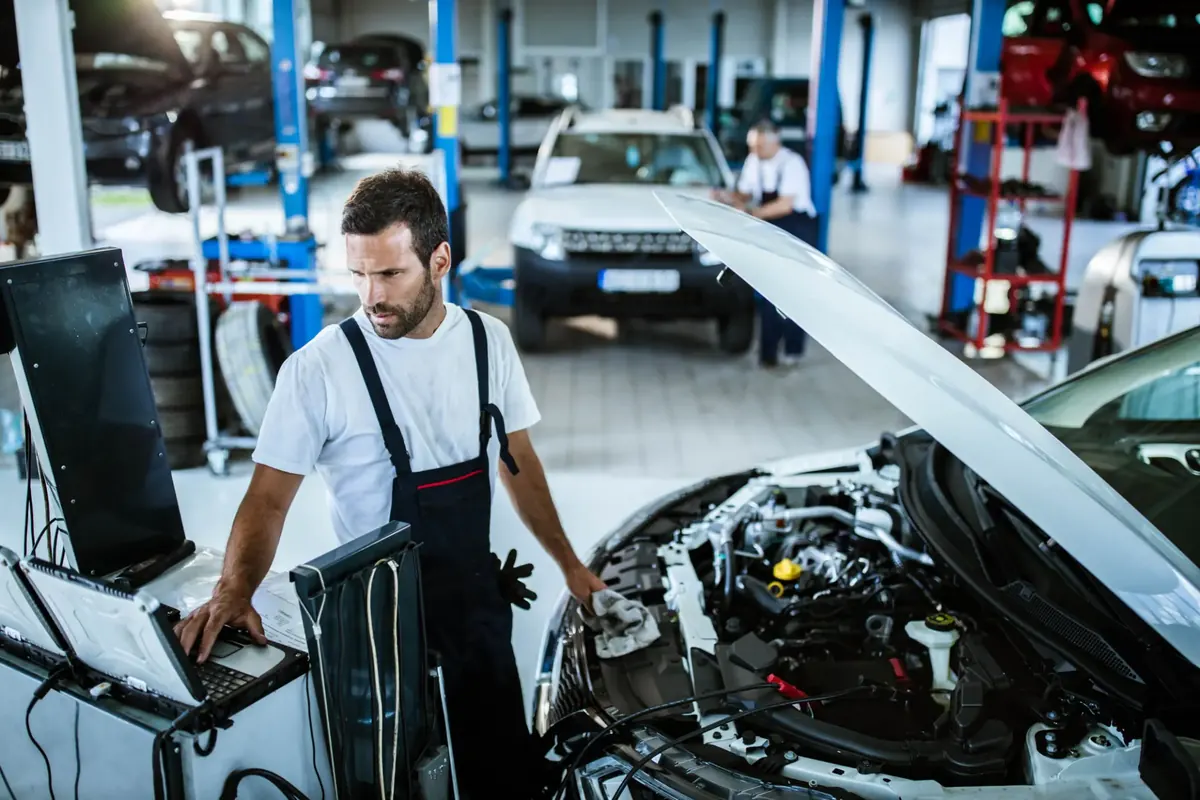 Technician using diagnostic equipment beside an engine bay