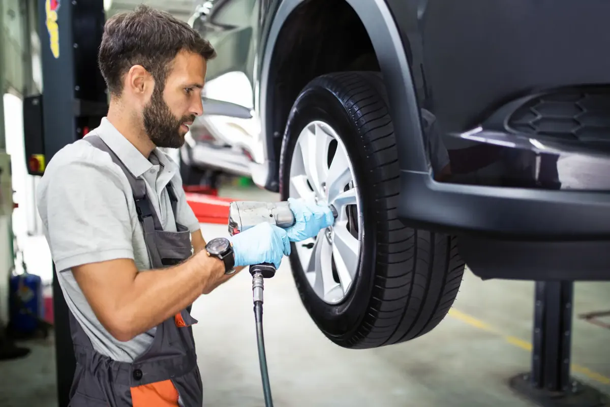 Technician fitting a wheel and tire to a raised vehicle